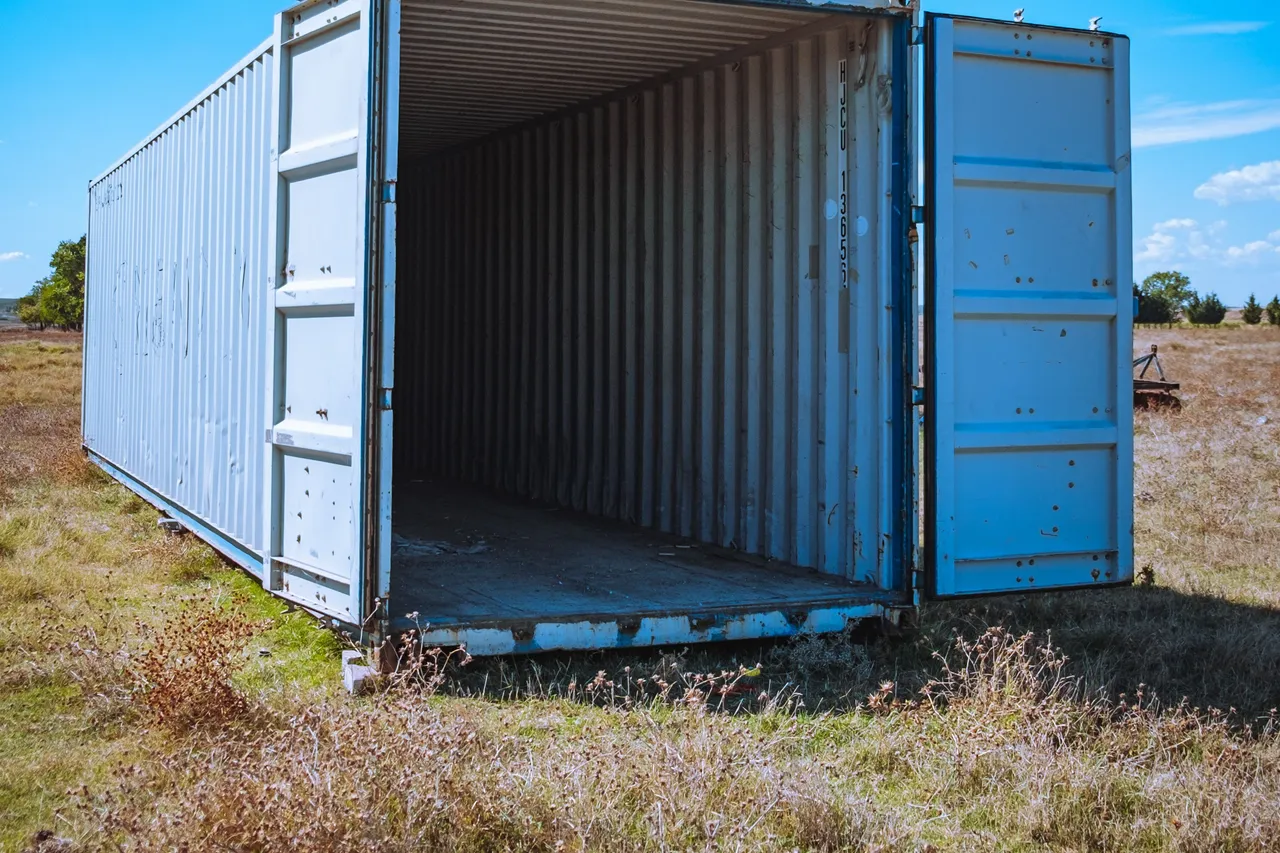 Shipping container standing in a grass field with both doors open
