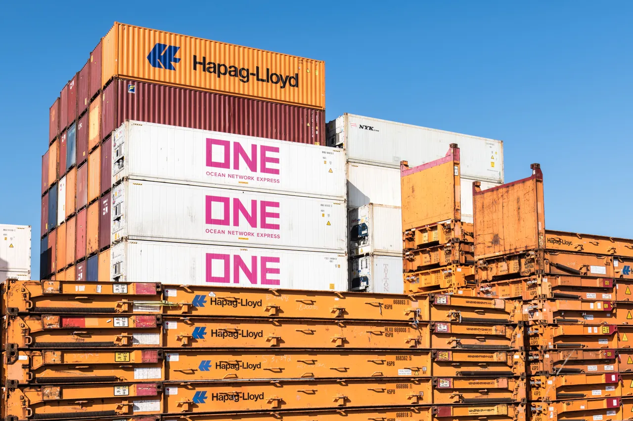 Stacked refrigerated shipping containers beside rows of folded container chassis