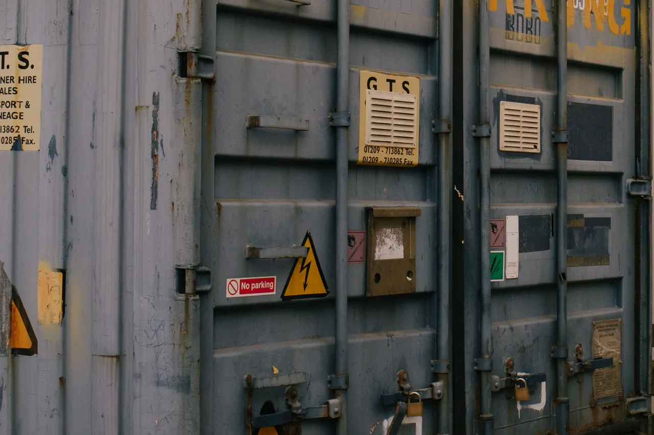 Close-up of weathered shipping container doors showing hinges, locking bars, vents and warning placards