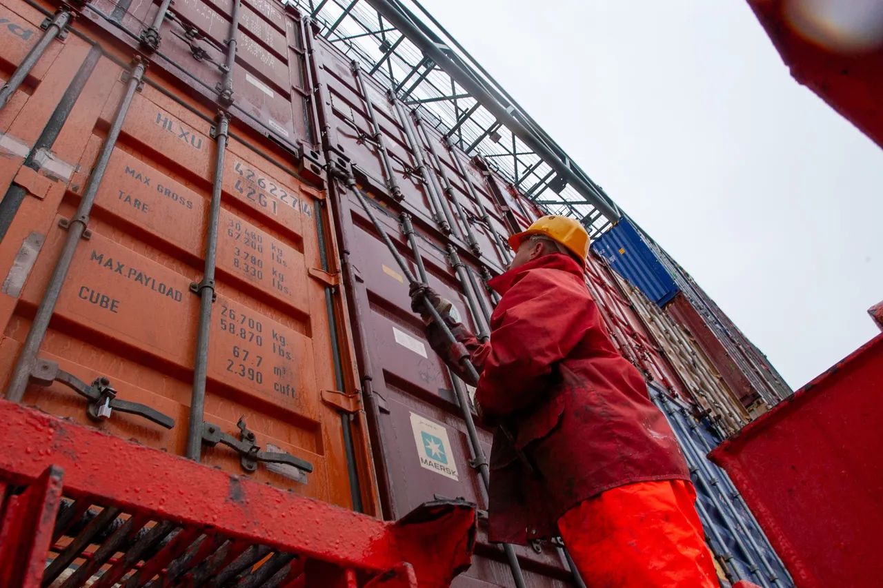 Worker in red protective clothing and hard hat climbing alongside a stack of shipping containers